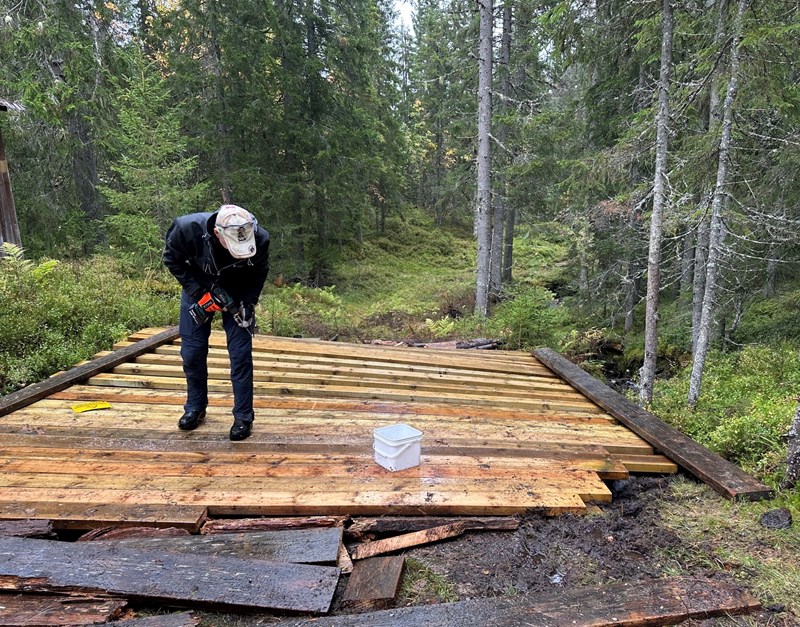 Lars Petter skrur fast plank. Og vi ser at det må hentes inn flere planker for å få tett bru. Foto: Trond Urdal. Lars Petter skrur fast plank. Og vi ser at det må hentes inn flere planker for å få tett bru. Foto: Trond Urdal.